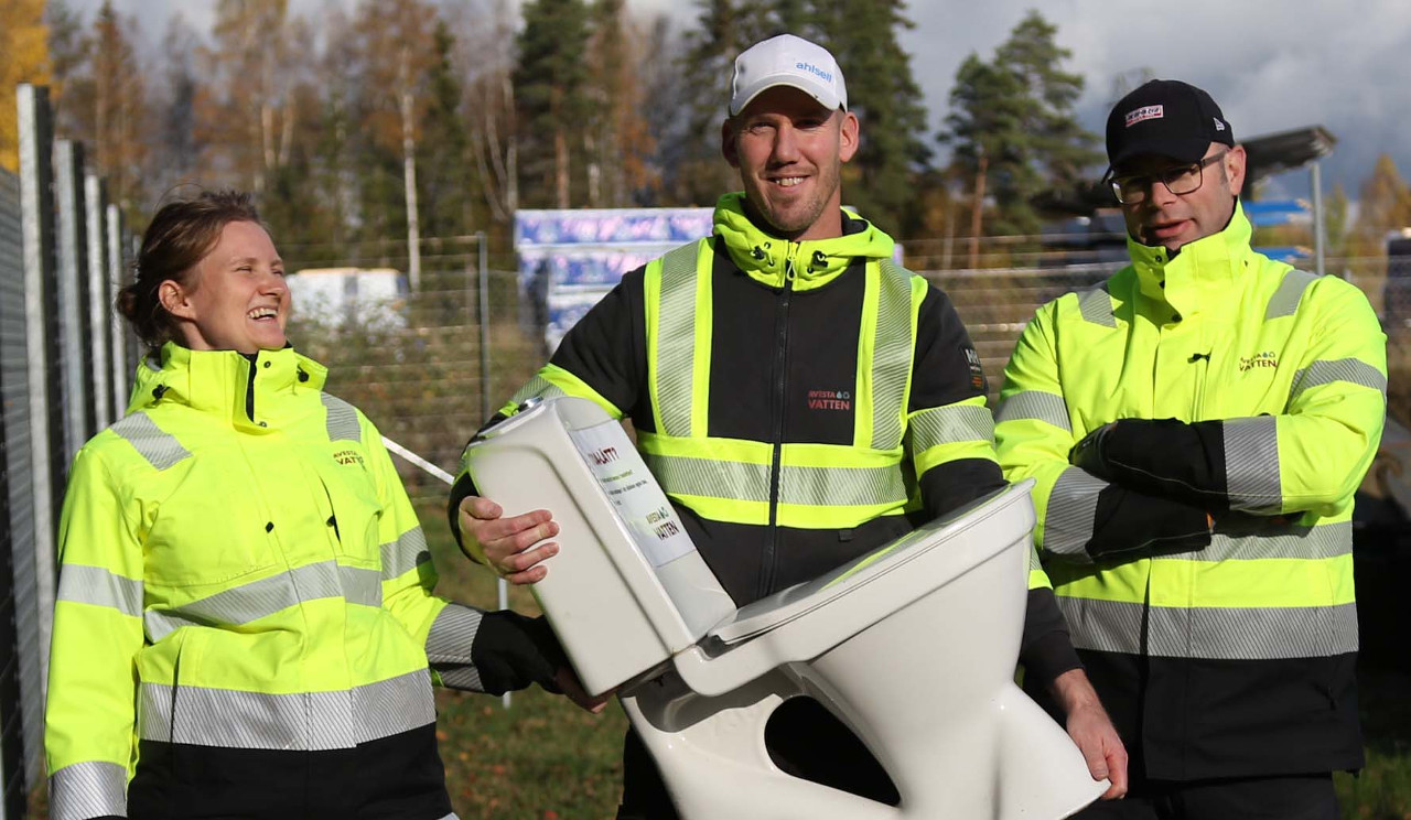 tre glada personer varav en håller i en toalettstol