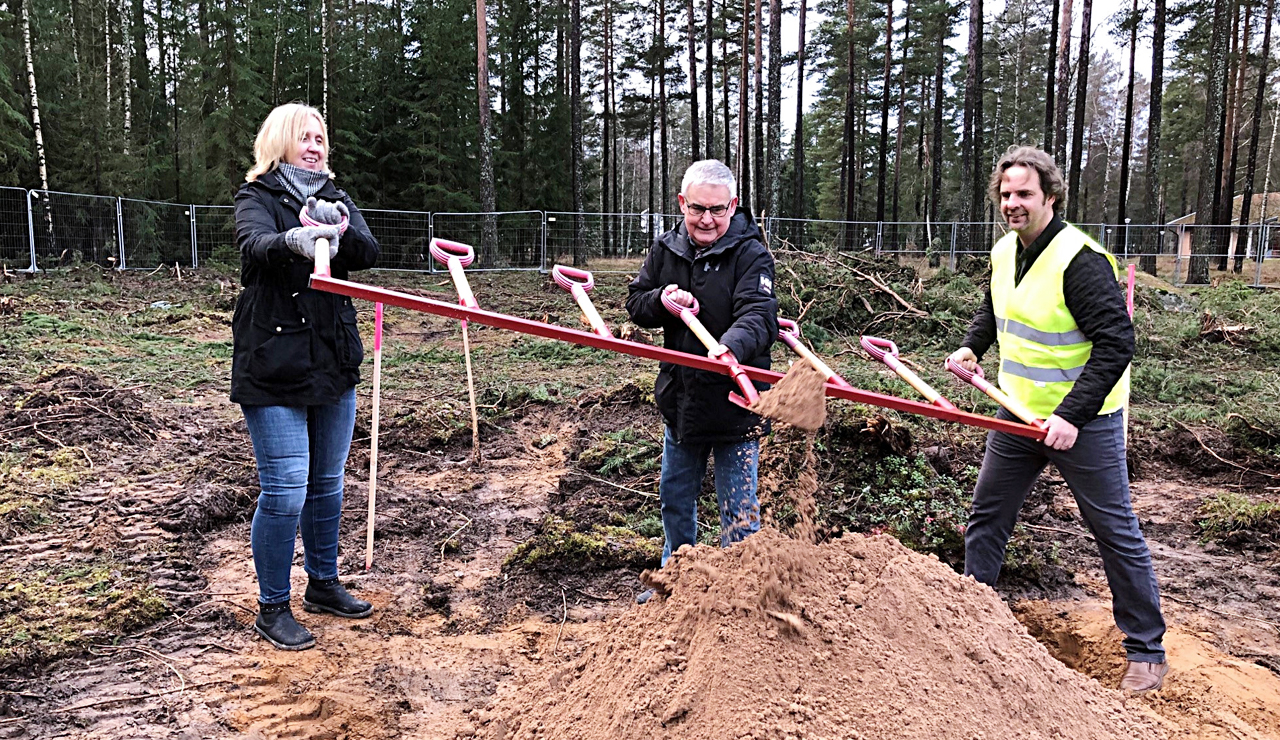 Trepersoner tar ett gemensamt spadtag och lyfter så jord och sand ryker.