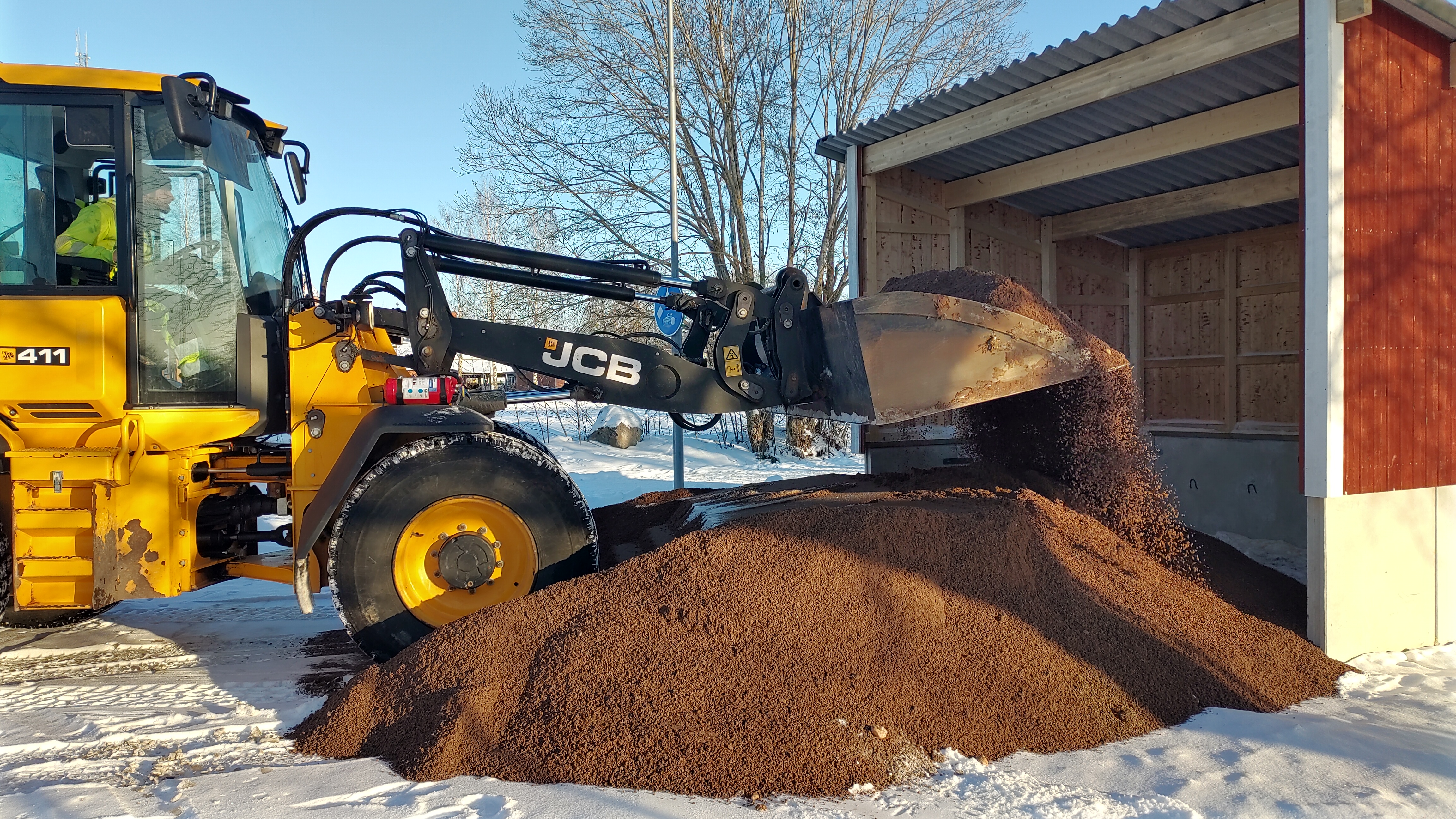 grävmaskin som skyfflar sand in i ett litet hus
